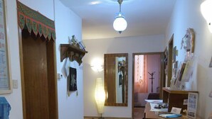 Una sala de estar con piso de madera, ventilador de techo, alfombra, estantería y escritorio con papeles.