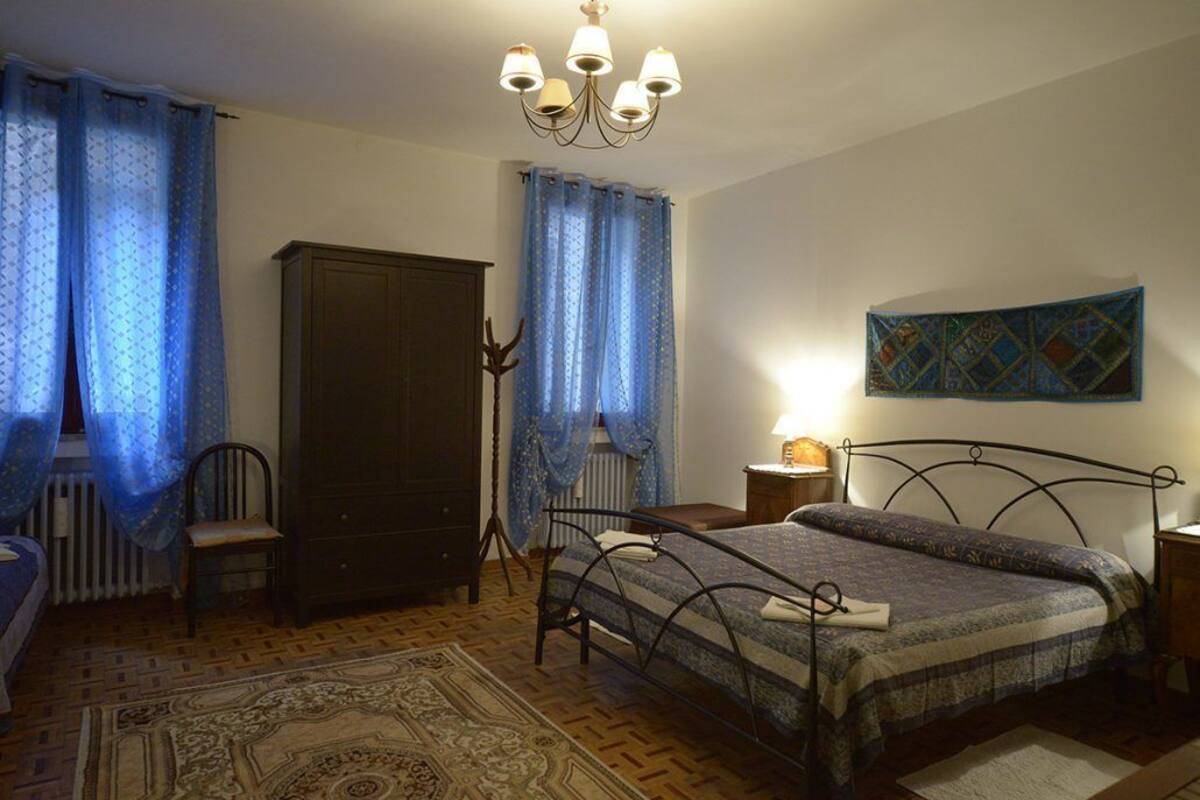 Quarto com cama, guarda-roupa, cadeira, radiador, candelabro e um quadro na parede.