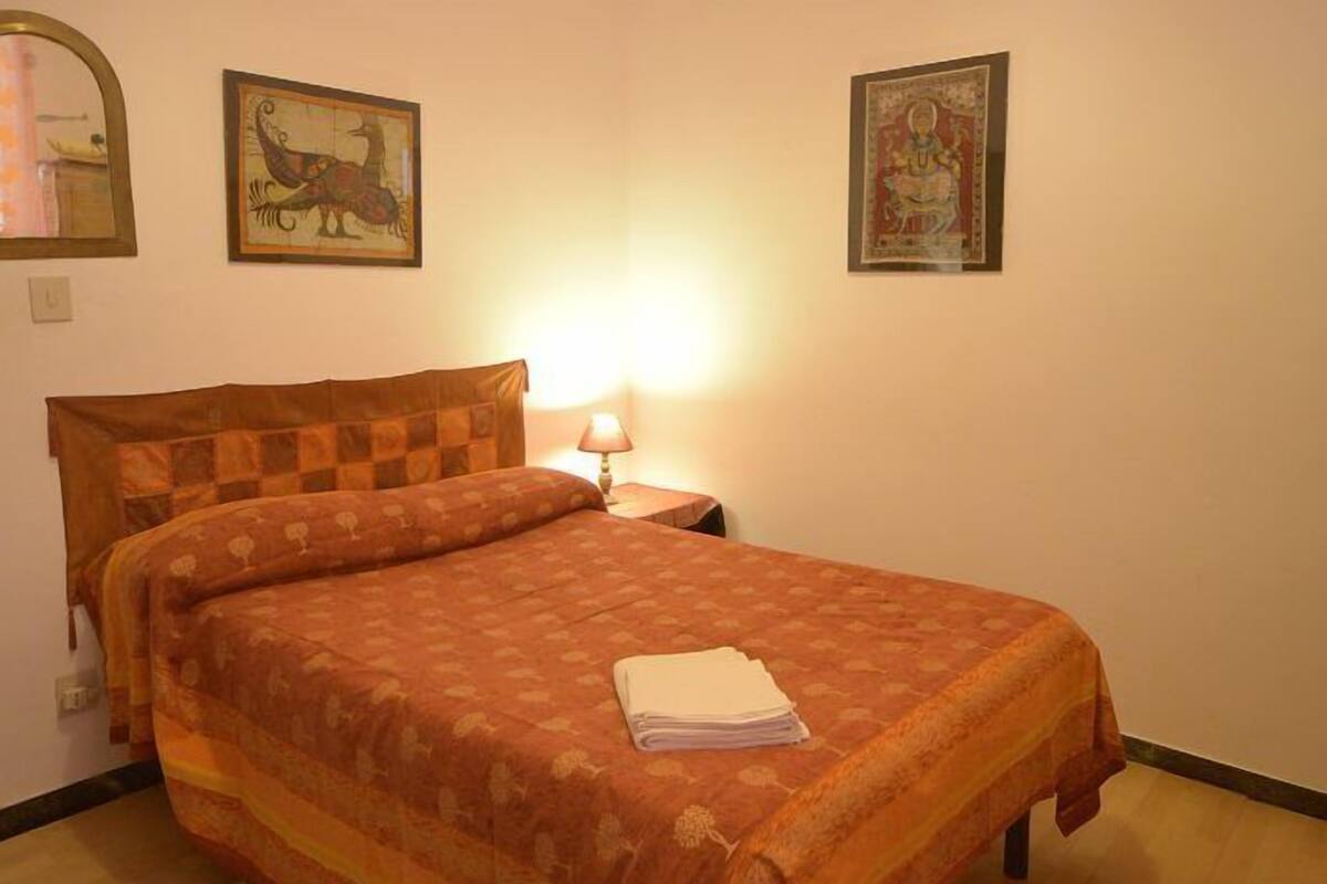 Uma cama de solteiro com colcha xadrez, uma luminária de cabeceira e duas fotos emolduradas na parede.