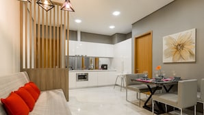 A modern kitchen with white cabinets, a dining area with a table and chairs, and a sofa with red cushions. - Soho Suites KLCC By Aloha (Kuala Lumpur)