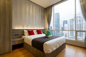 Quarto de hotel moderno com uma cama grande, mesa de cabeceira e vista para a cidade através de uma janela ampla.