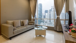 A modern living room with a sofa, a glass coffee table, and a view of a cityscape through large windows. - Soho Suites KLCC By Aloha (Kuala Lumpur)