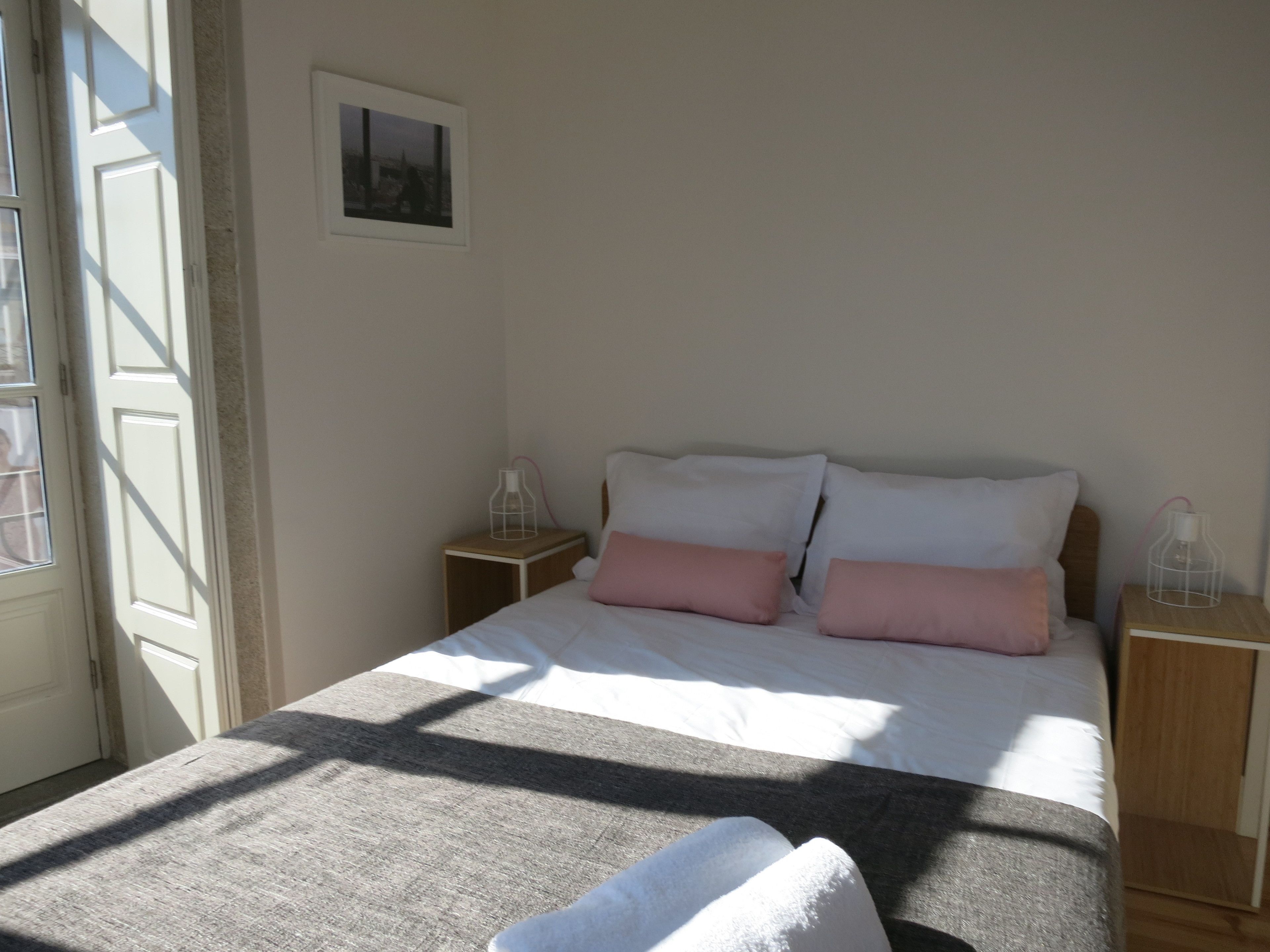 Un dormitorio con cama, almohadas, una mesita de noche y un cuadro en la pared.