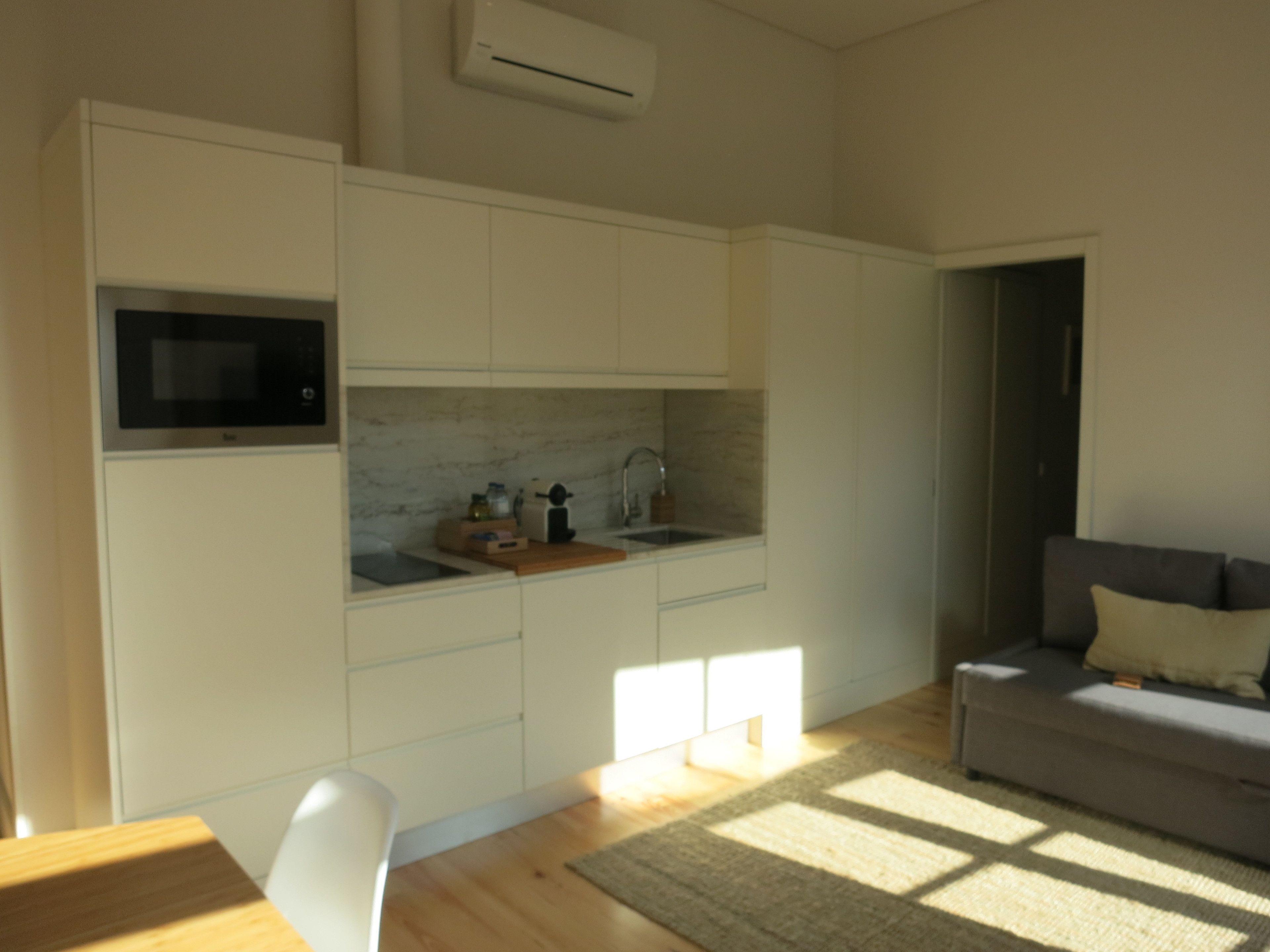 A compact kitchen with white cabinetry, a microwave, and a sink. There's a gray sofa and a wooden table in the living area.