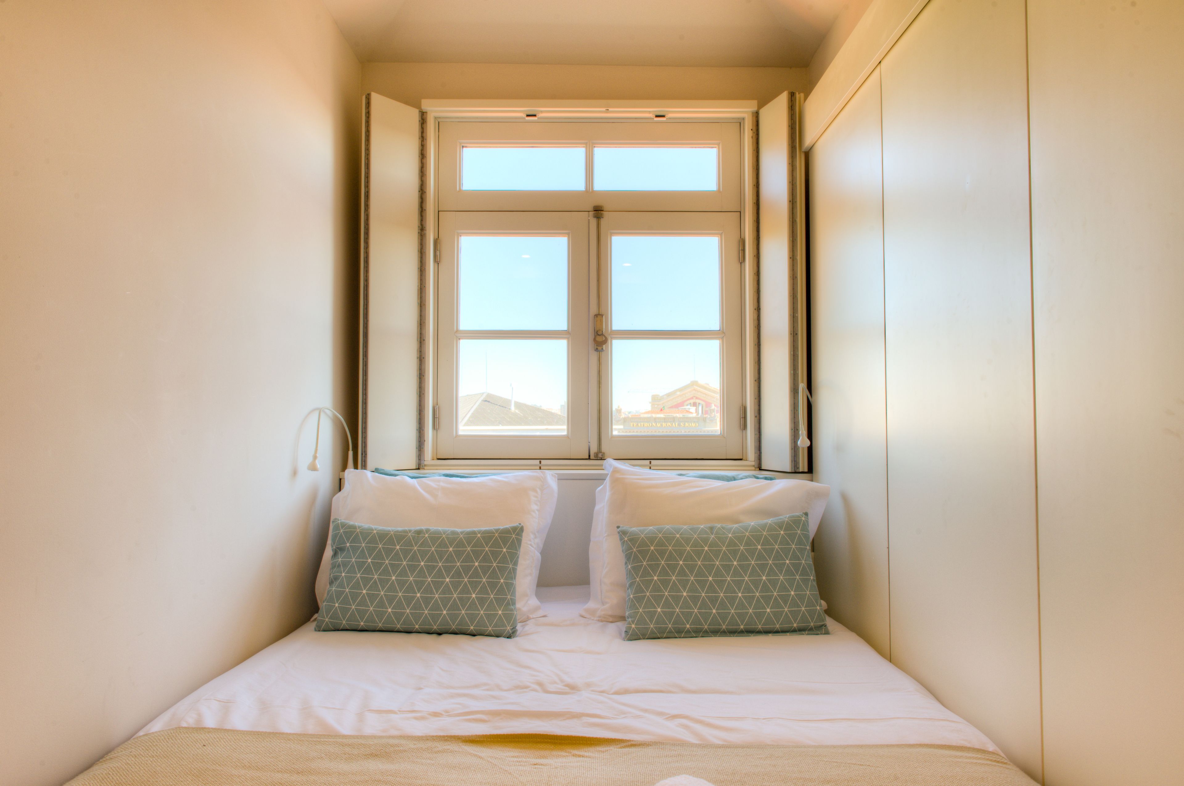 A small, narrow room with a bed, two pillows, and a window.