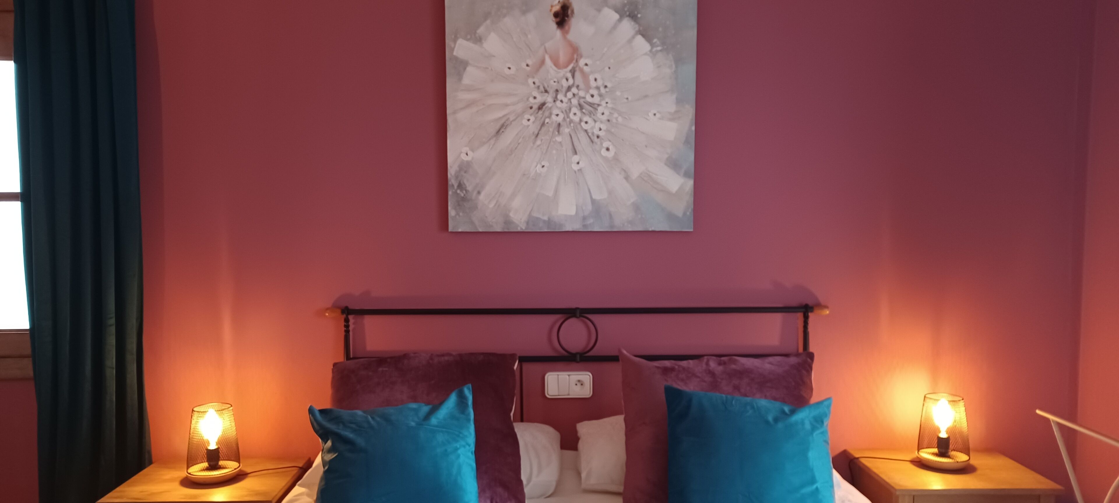 A bedroom with a bed, two bedside lamps, a headboard, and a wall-mounted artwork.