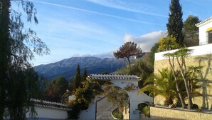 A paved courtyard with a stone wall, a white archway, and a view of mountains in the background.