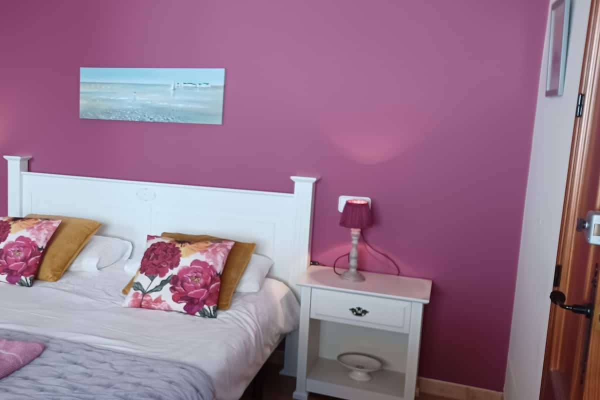 A bedroom with a bed, two nightstands, a mirror, and a wall-mounted picture.