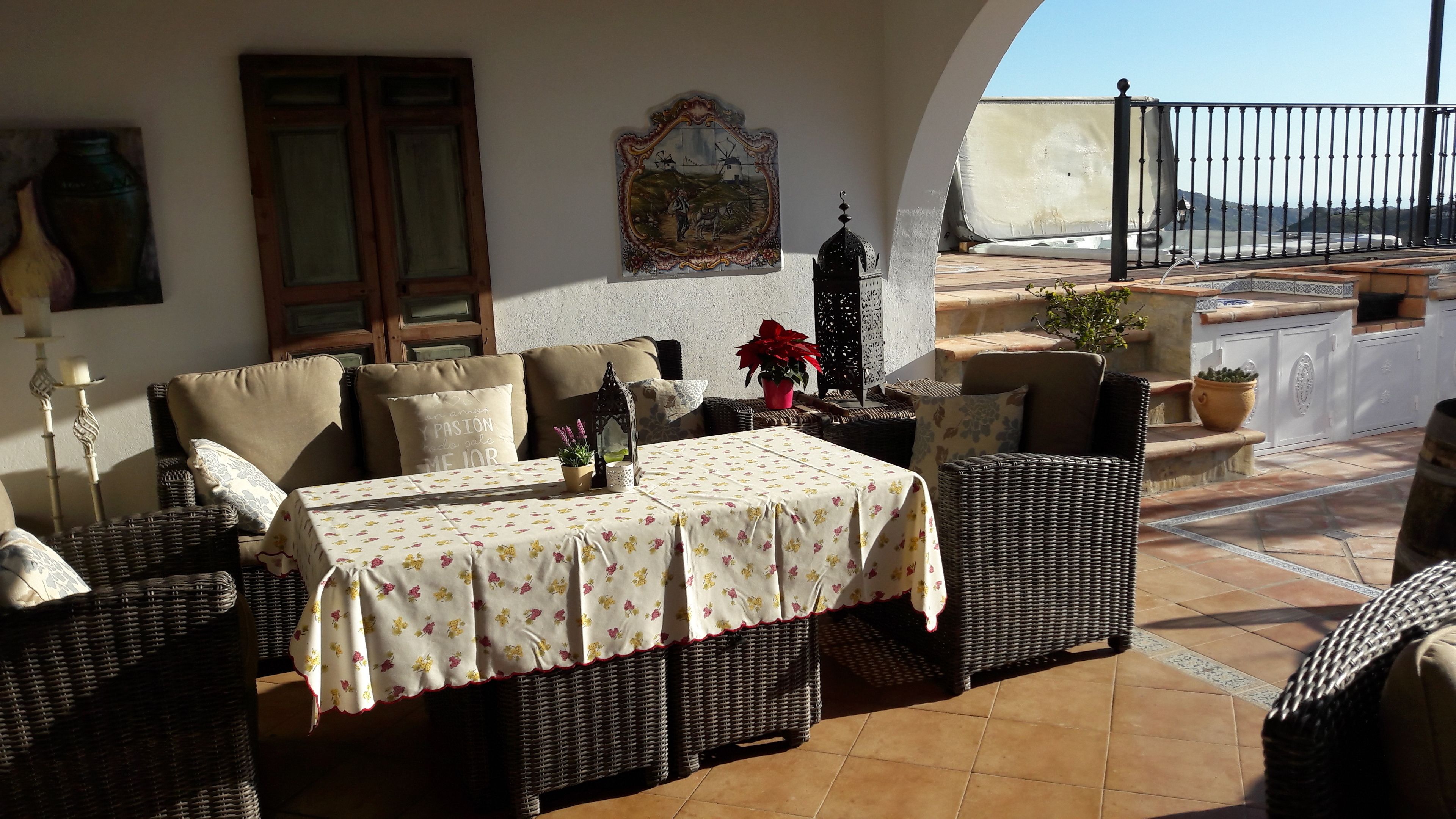 Un patio al aire libre con mobiliario de mimbre, una mesa con mantel floral y una planta en maceta.