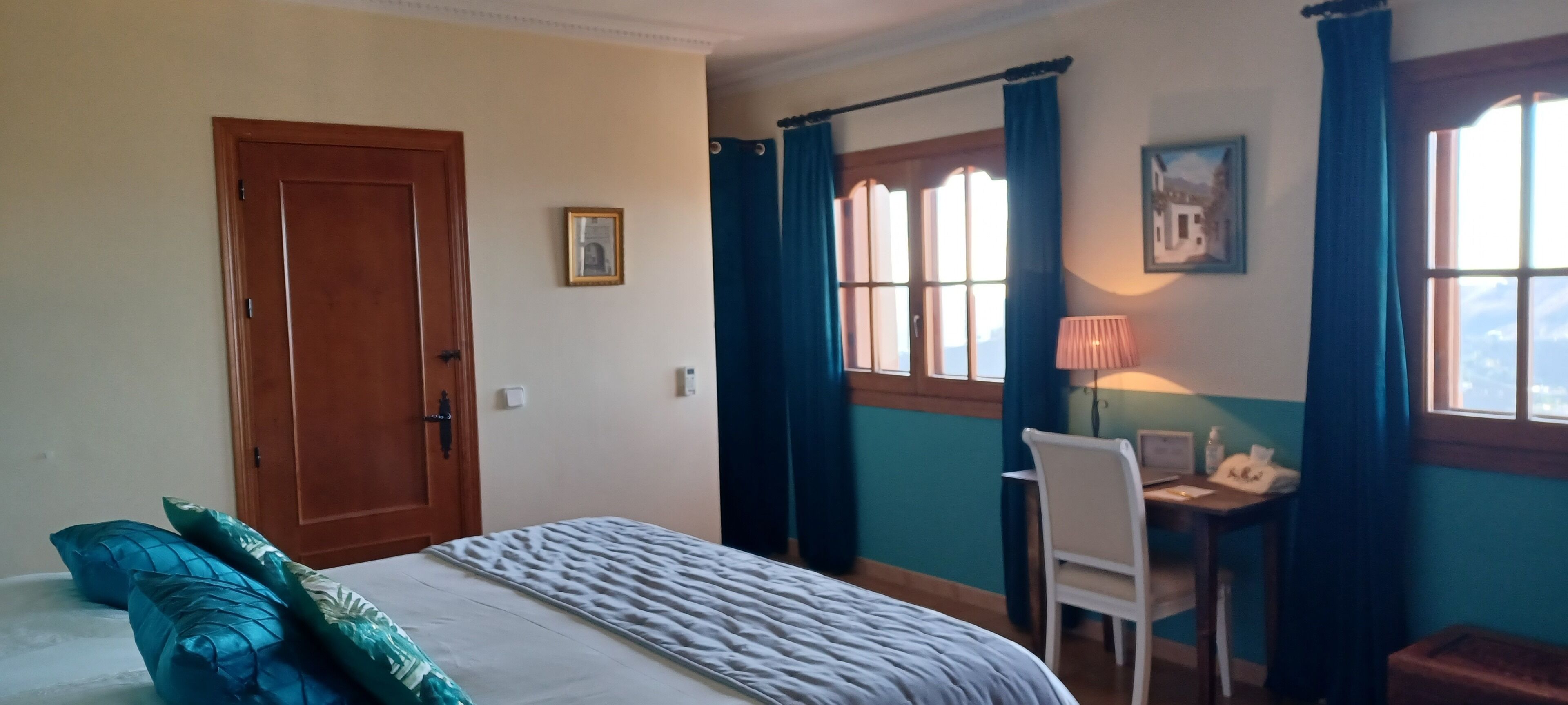 A room with a bed, a desk with a chair, a lamp, and a window with curtains.