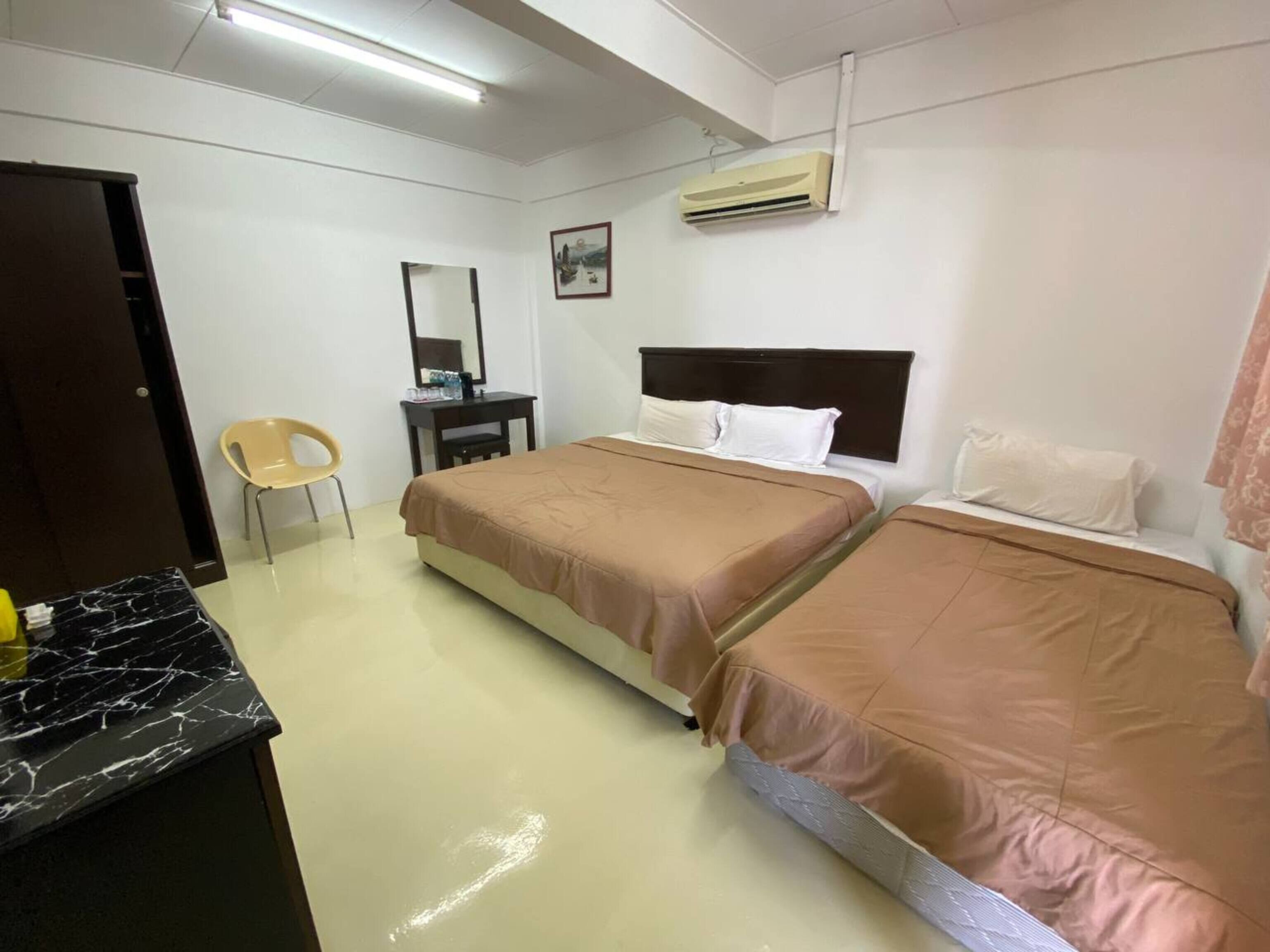 A hotel room with two beds, a desk, a chair, a mirror, and an air conditioning unit.