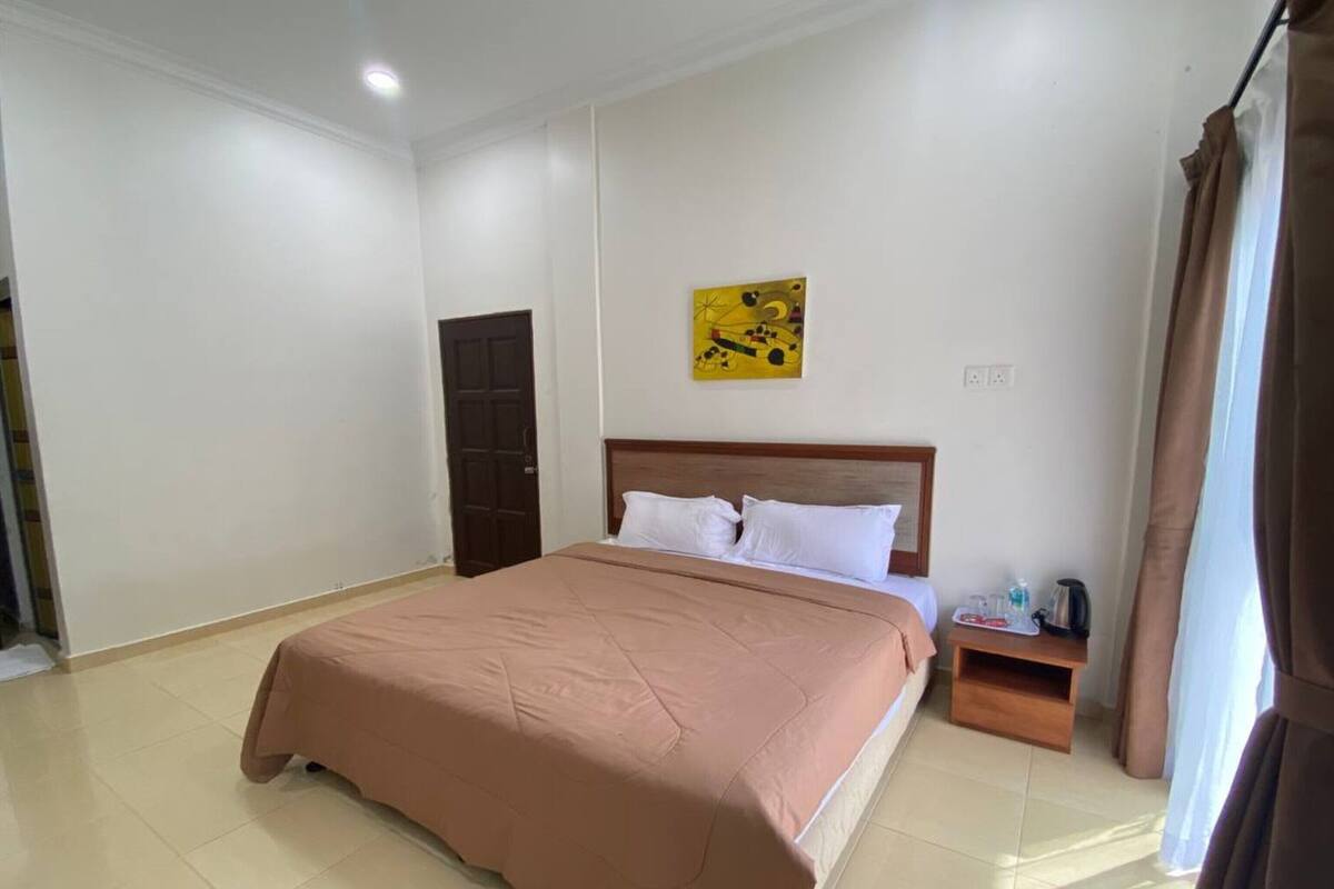 A hotel room with a large bed, a nightstand, a painting on the wall, and a door.