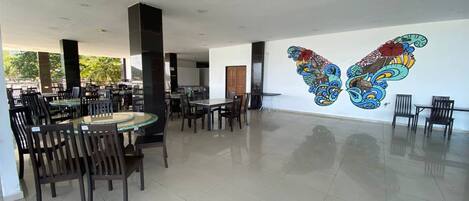 A spacious indoor dining area with multiple tables and chairs, a large mural on the wall, and a tiled floor.