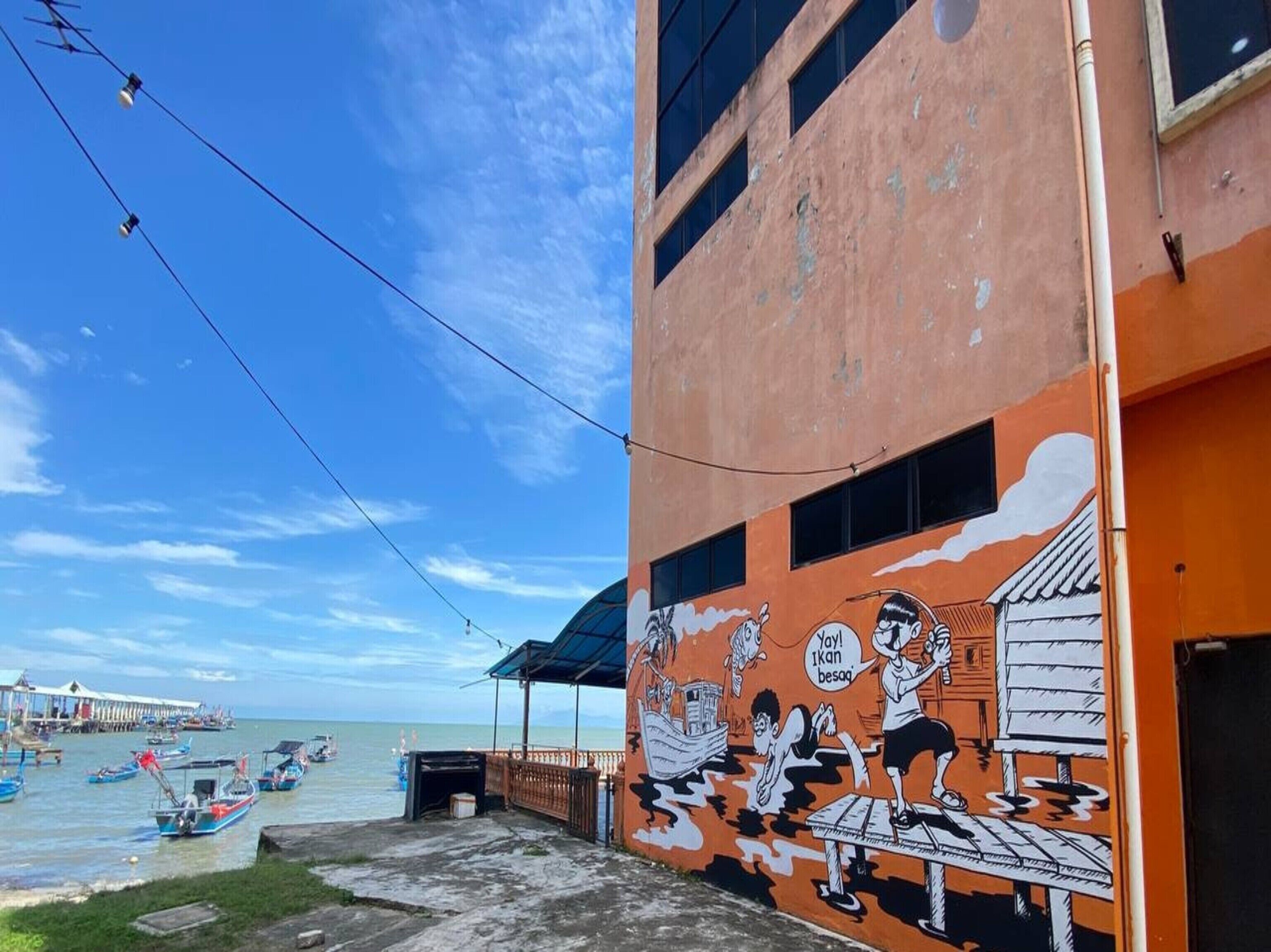A coastal building with a mural depicting a beach scene, including boats and people.