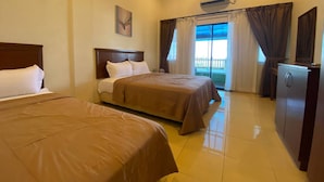 Habitación de hotel con dos camas, ventilador de techo, aire acondicionado, un refrigerador pequeño y una ventana con cortinas.