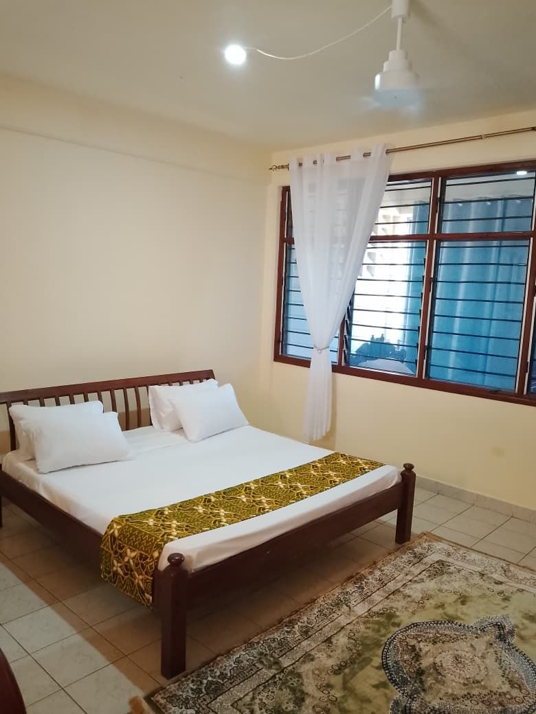 Ein Schlafzimmer mit Bett, Fenster mit Vorhängen, Deckenventilator und Teppich mit Muster.