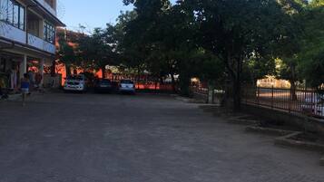 A street scene with a building on the left, a tree in the center, and a fence on the right.