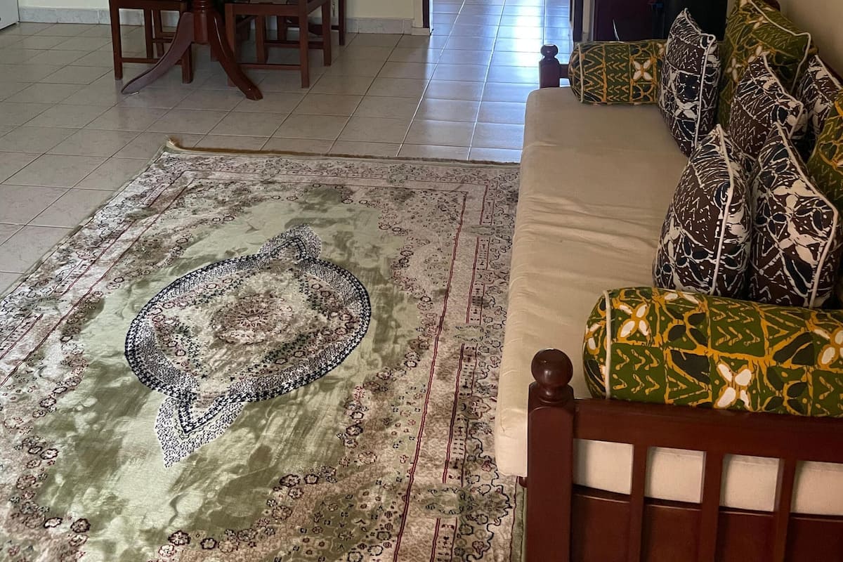 Un salon comprenant un canapé, une table à manger avec des chaises, un tapis à motifs et un distributeur d’eau.