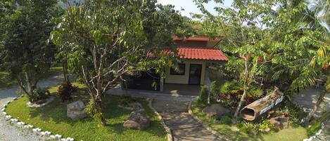 A building with a red roof, surrounded by a garden with trees and a gravel path.