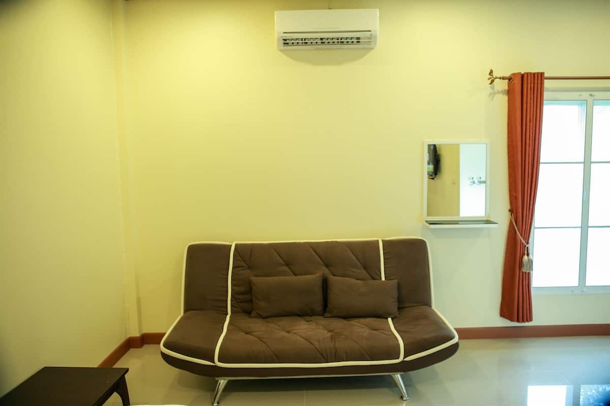 A room with a brown sofa, a small table, a mirror, and a window with curtains.