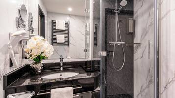 A modern bathroom with a glass-enclosed shower, a sink with a marble countertop, and a vase with white flowers.
