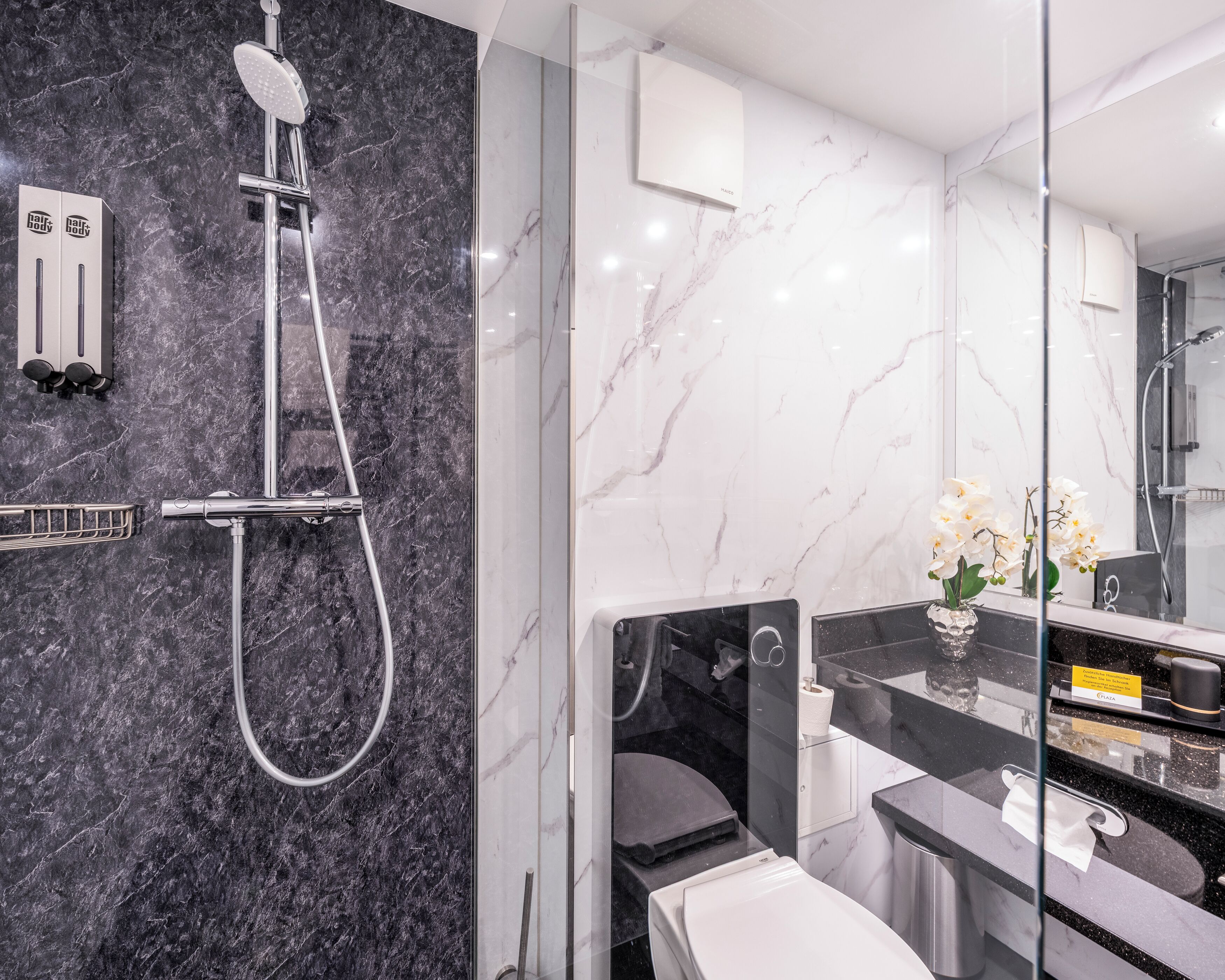 Un baño moderno con cabina de ducha de vidrio, pared de mármol, inodoro y lavamanos con espejo.