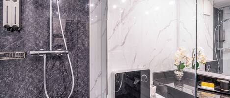 Un baño moderno con cabina de ducha de vidrio, pared de mármol, inodoro y lavamanos con espejo.
