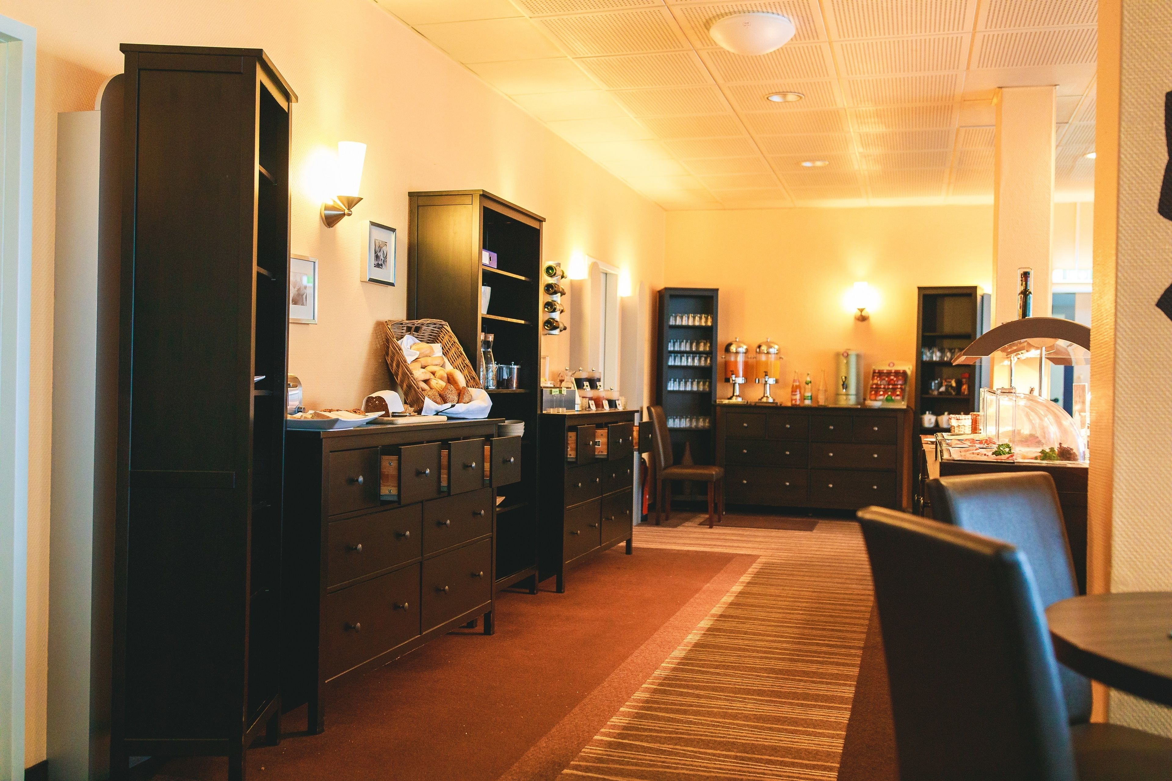 Une chambre d’hôtel dotée d’une grande armoire, d’un bureau avec une chaise, d’une table à manger et d’un coin cuisine avec des placards et des appareils électroménagers.