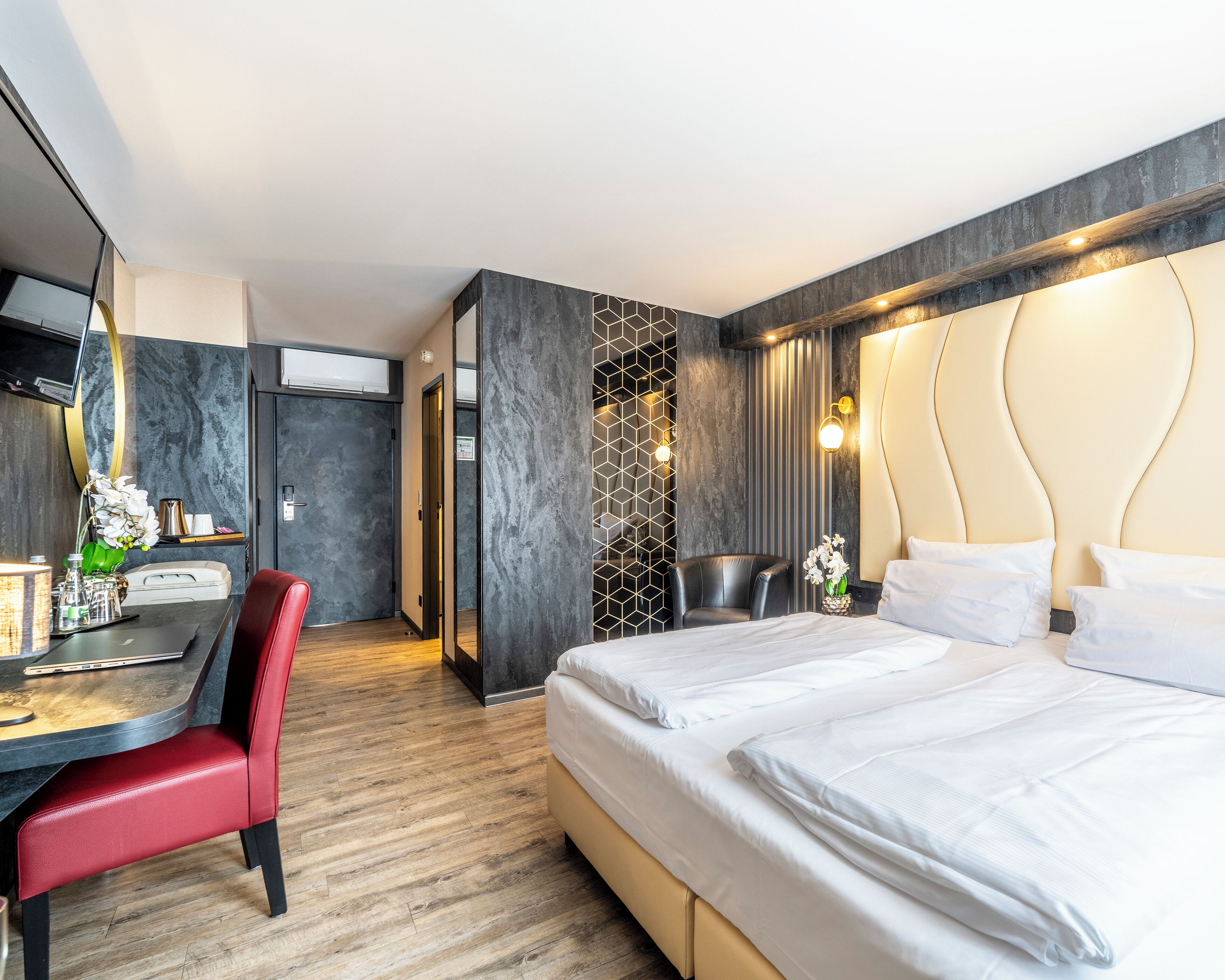 A modern hotel room with a bed, desk, chair, and a mirror.
