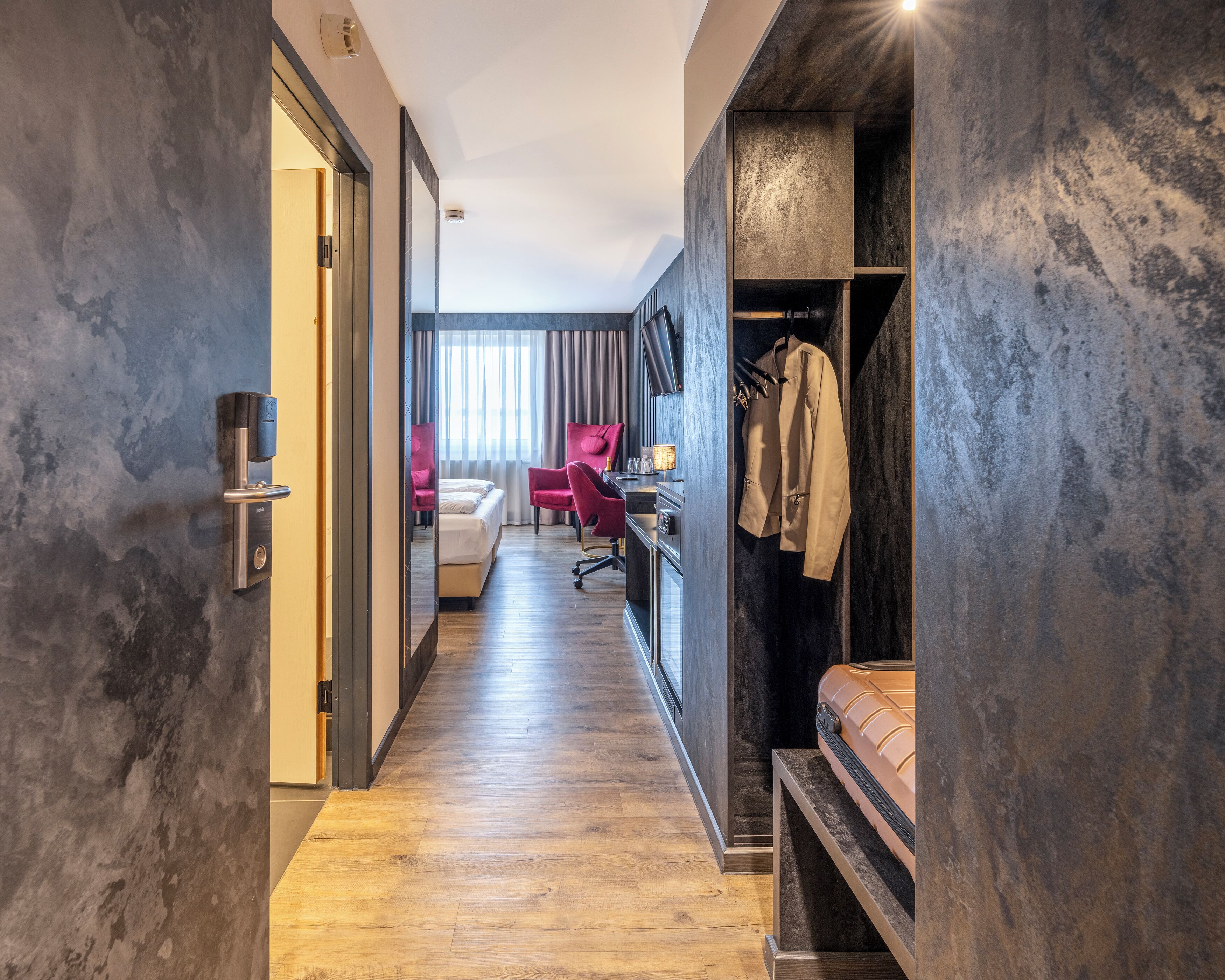 A hotel room with a bed, a desk, a chair, and a wardrobe.