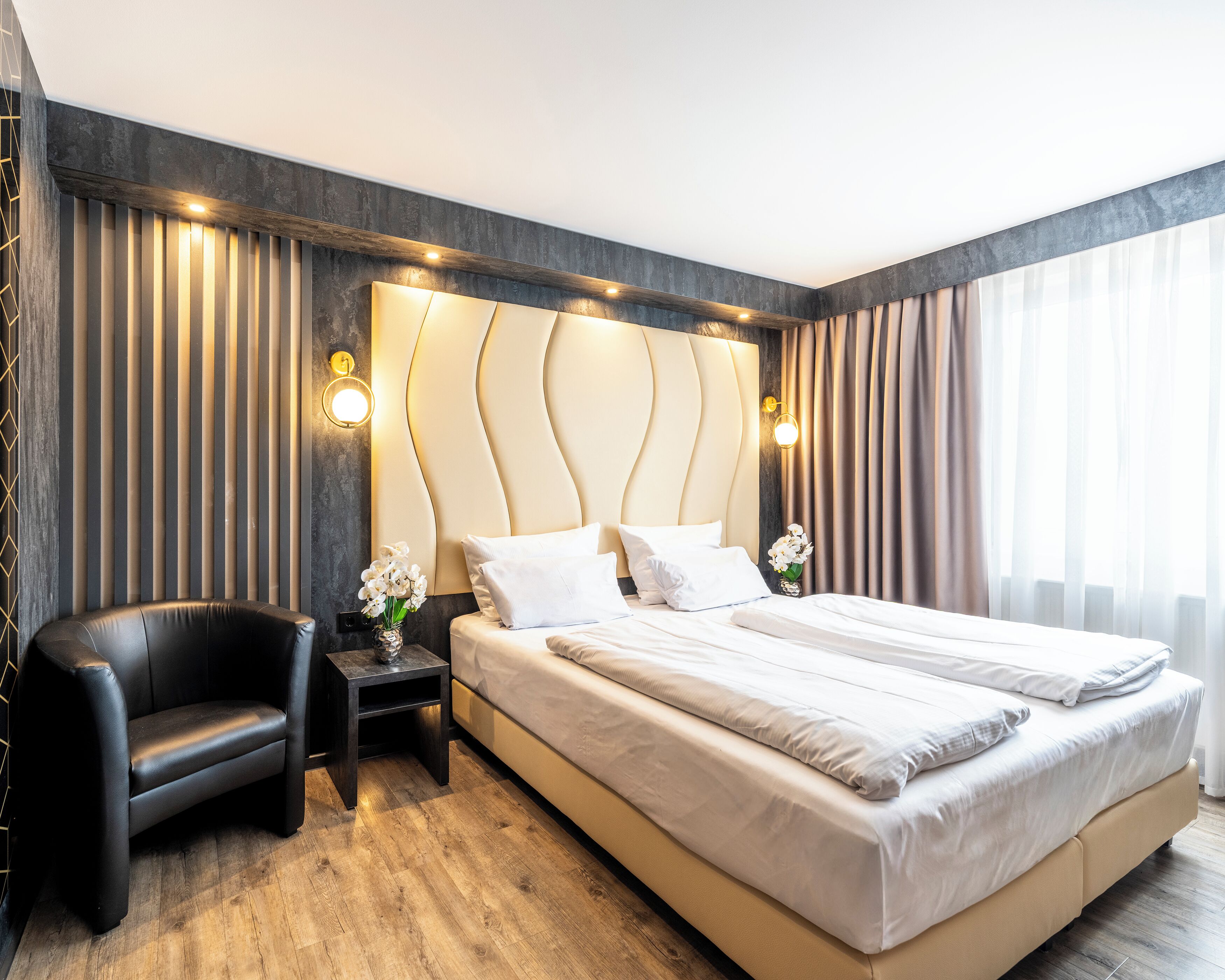 Une chambre d’hôtel moderne, dotée d’un grand lit, d’une chaise, d’une table de chevet et d’un luminaire fixé au mur.