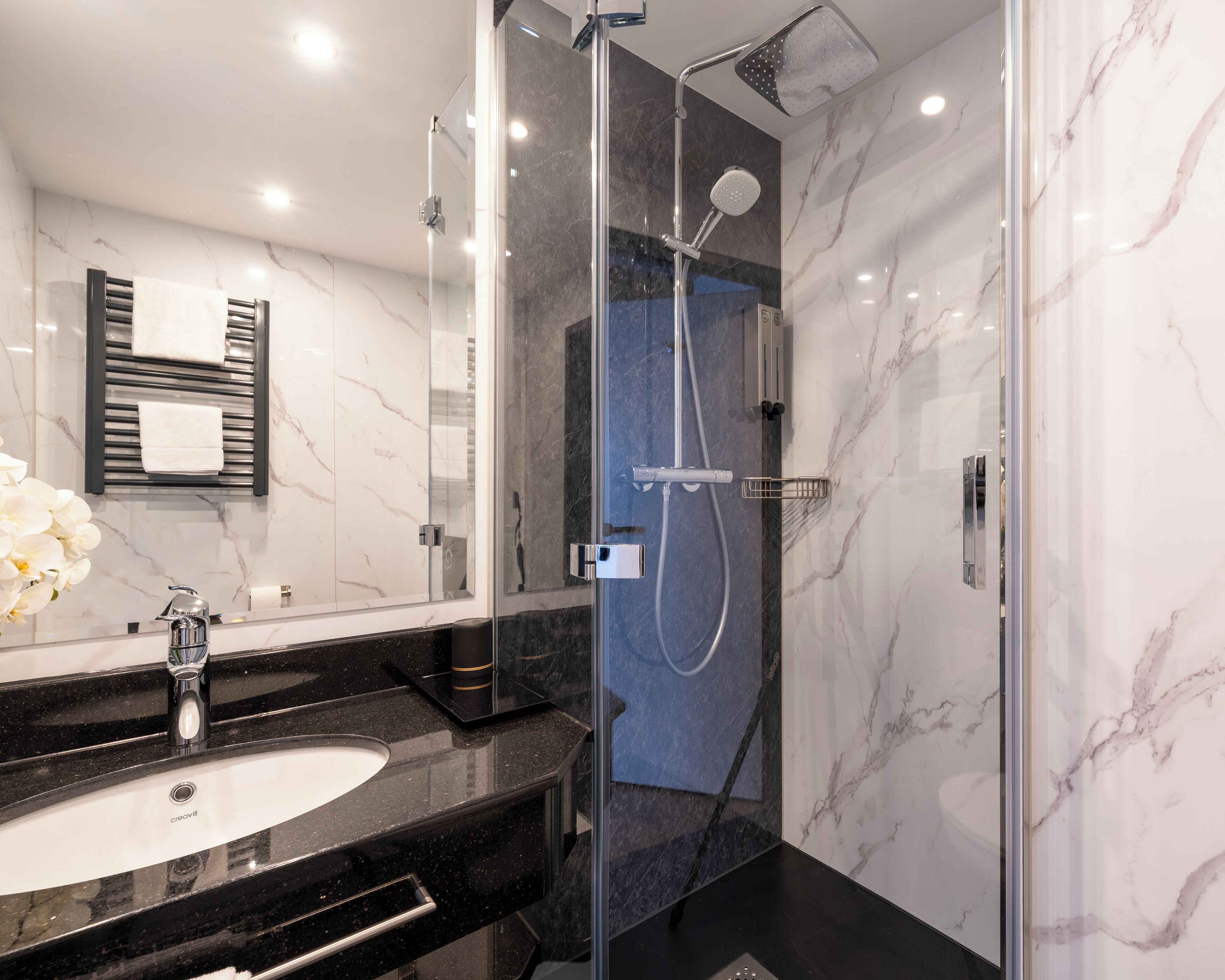 Een moderne badkamer met een douche met glazen wand, een zwarte marmeren wastafel en een witte wastafel.