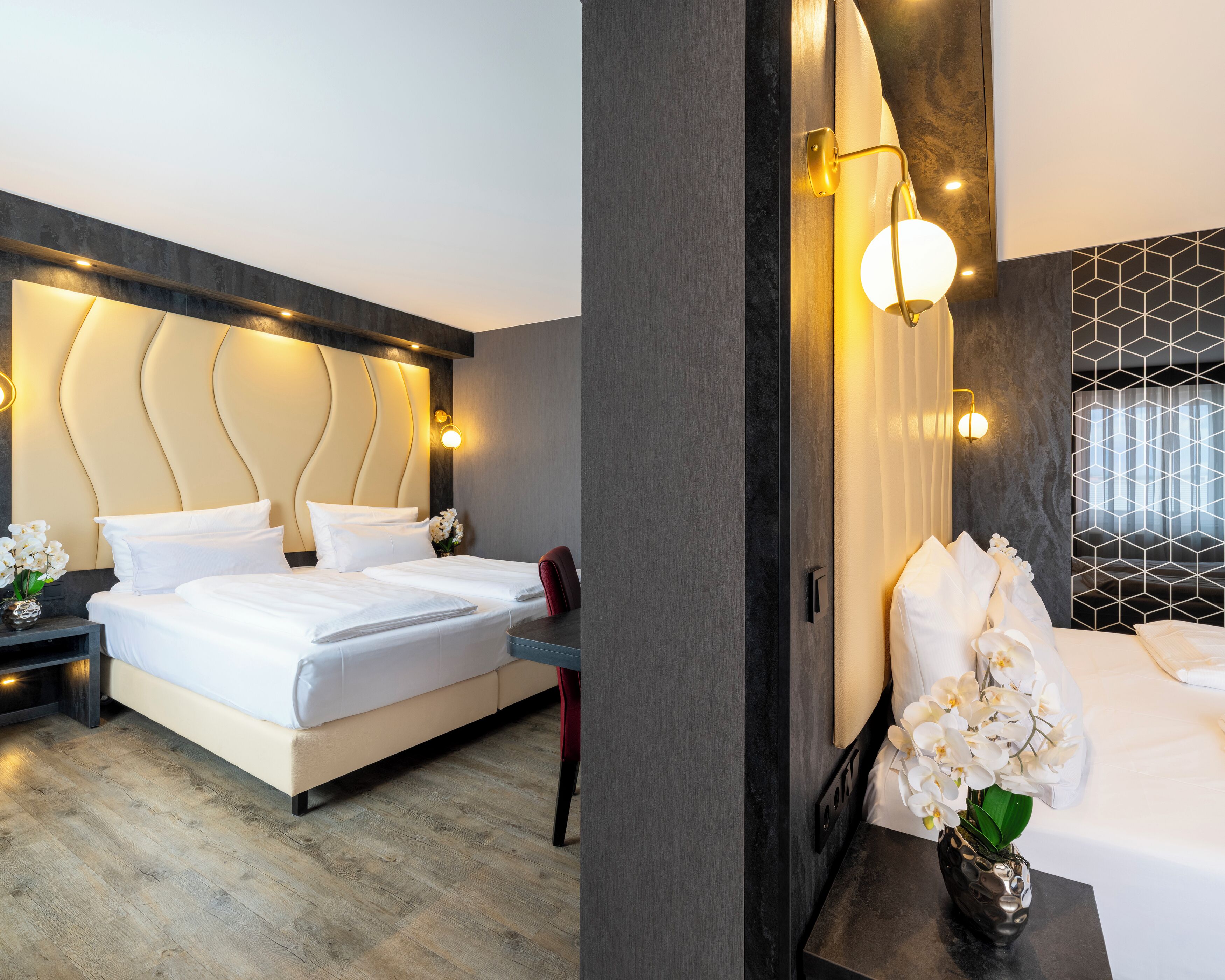 A modern hotel room with a large bed, bedside tables, a desk, and a decorative wall with geometric patterns.