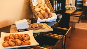 A breakfast buffet with bread, pastries, and a cutting board with a knife. - PLAZA INN Bruchsal (Bruchsal)