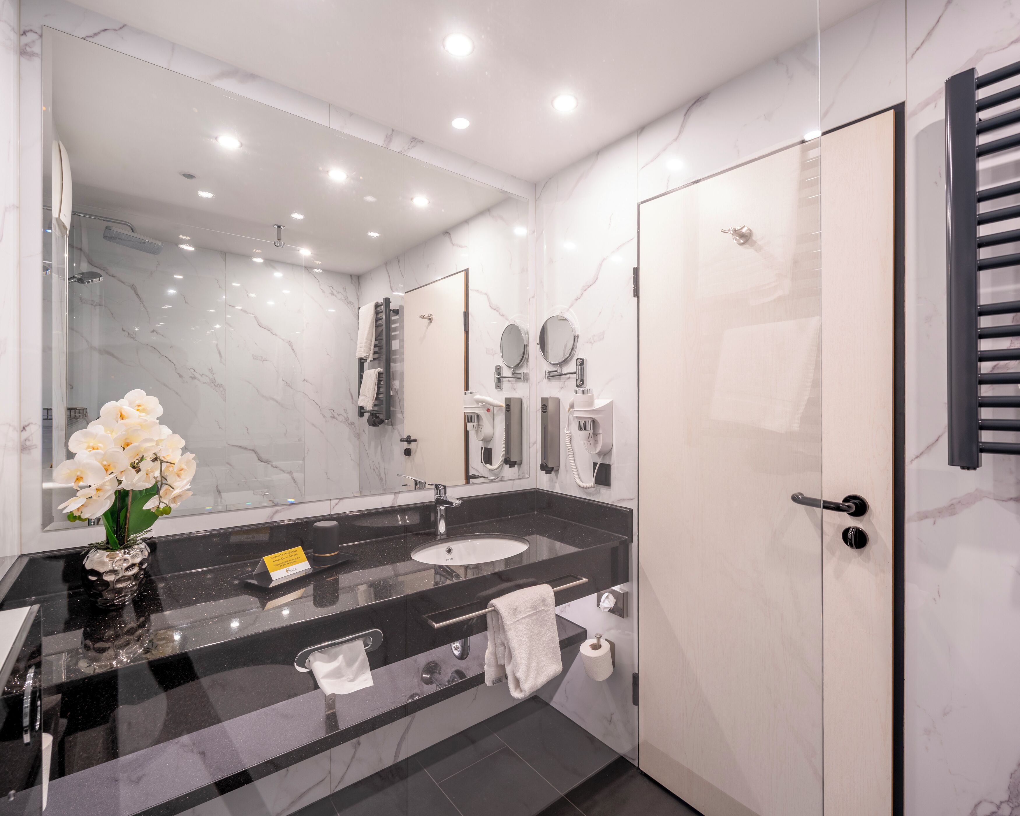 A modern bathroom with a marble vanity, a glass shower enclosure, and a towel rack.