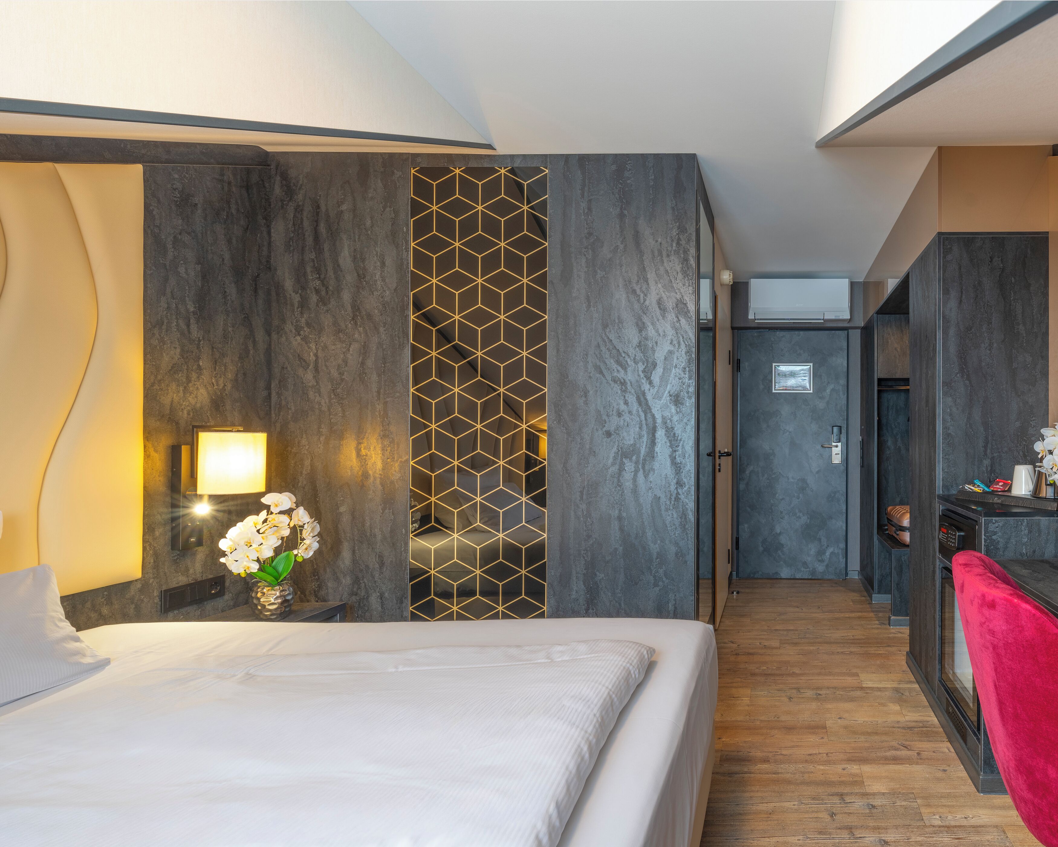 Une chambre d’hôtel avec un lit, une table de chevet avec une lampe, un panneau décoratif au mur et une vue sur le couloir.