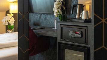 A hotel room with a bed, a desk with a laptop, a coffee maker, a minibar, and a wall-mounted TV.