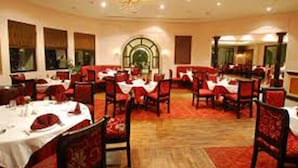 A dining area with round tables, red upholstered chairs, and a chandelier. - The White Lake Hotel (Tansen)
