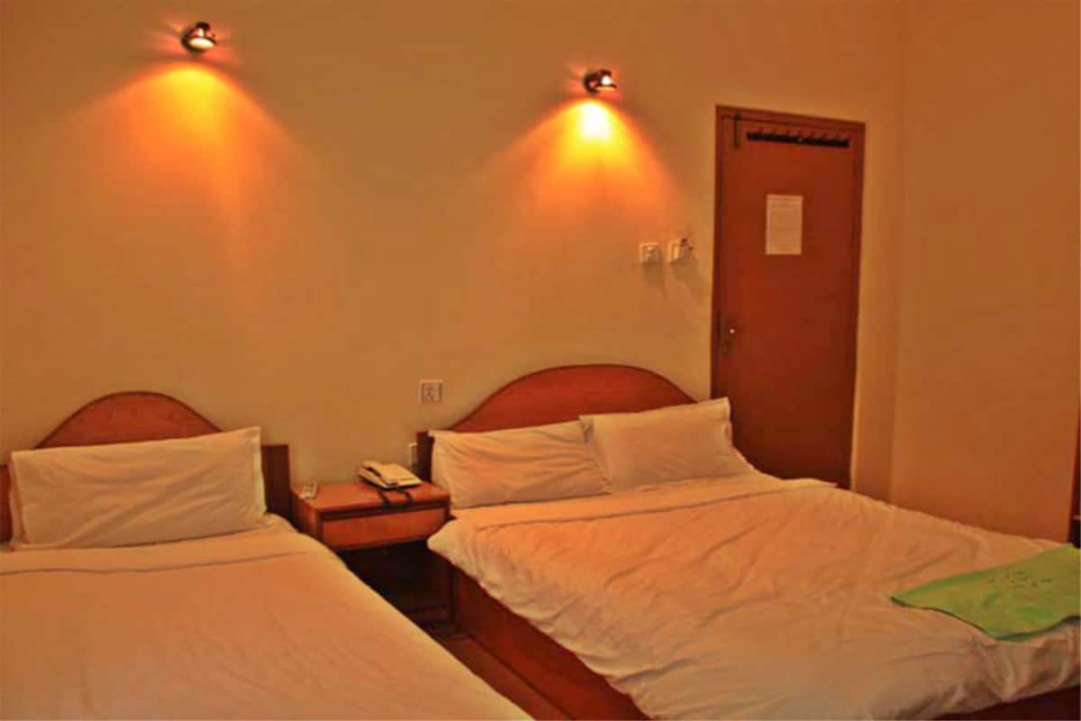 A hotel room with two single beds, a wooden headboard, a nightstand with a phone, and a door with a notice.