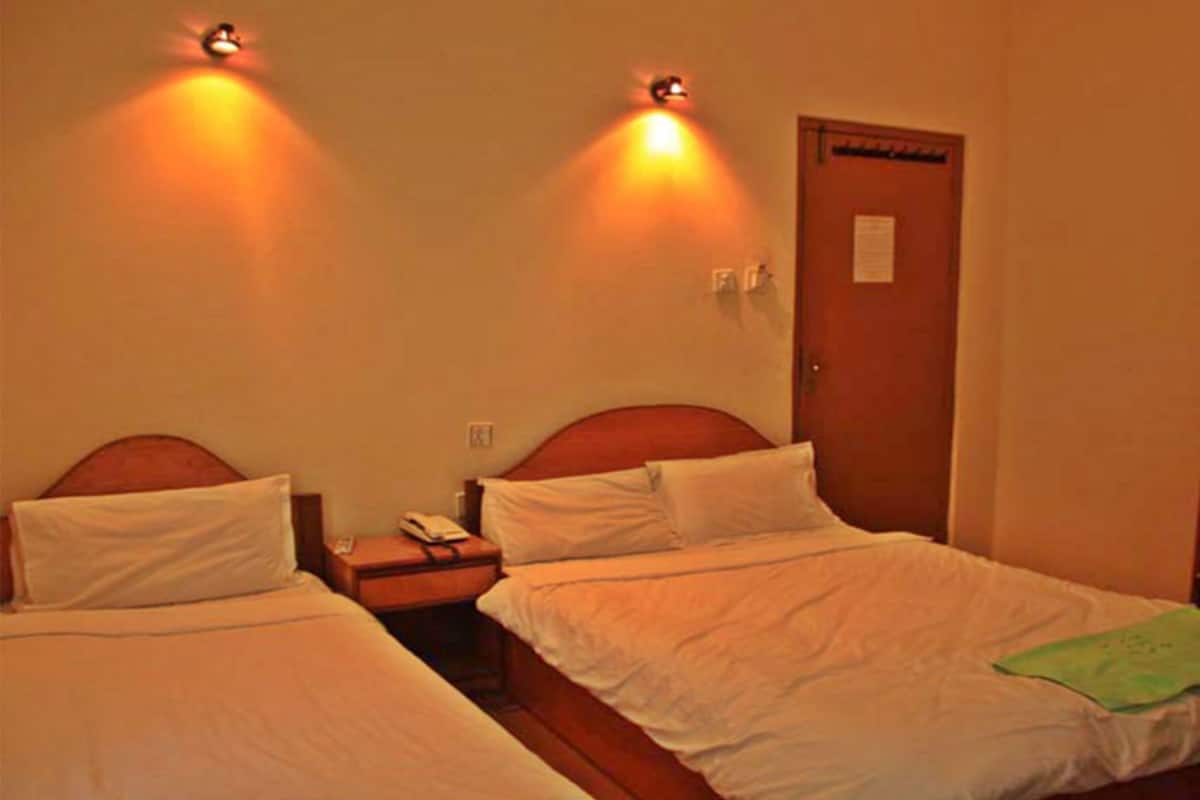 A hotel room with two single beds, a wooden headboard, a nightstand with a phone, and wall-mounted lights.