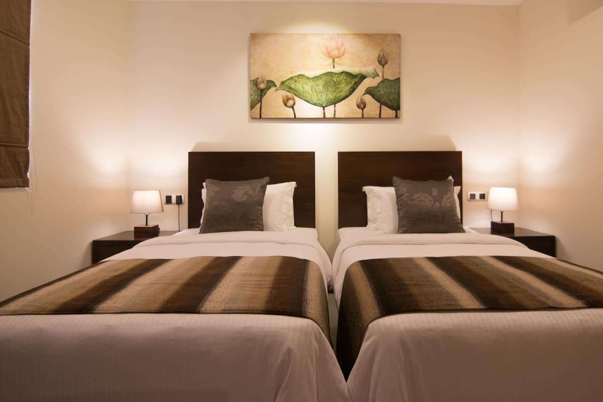 Une chambre d’hôtel avec deux lits, une tête de lit, des lampes de chevet et une œuvre d’art accrochée au mur.