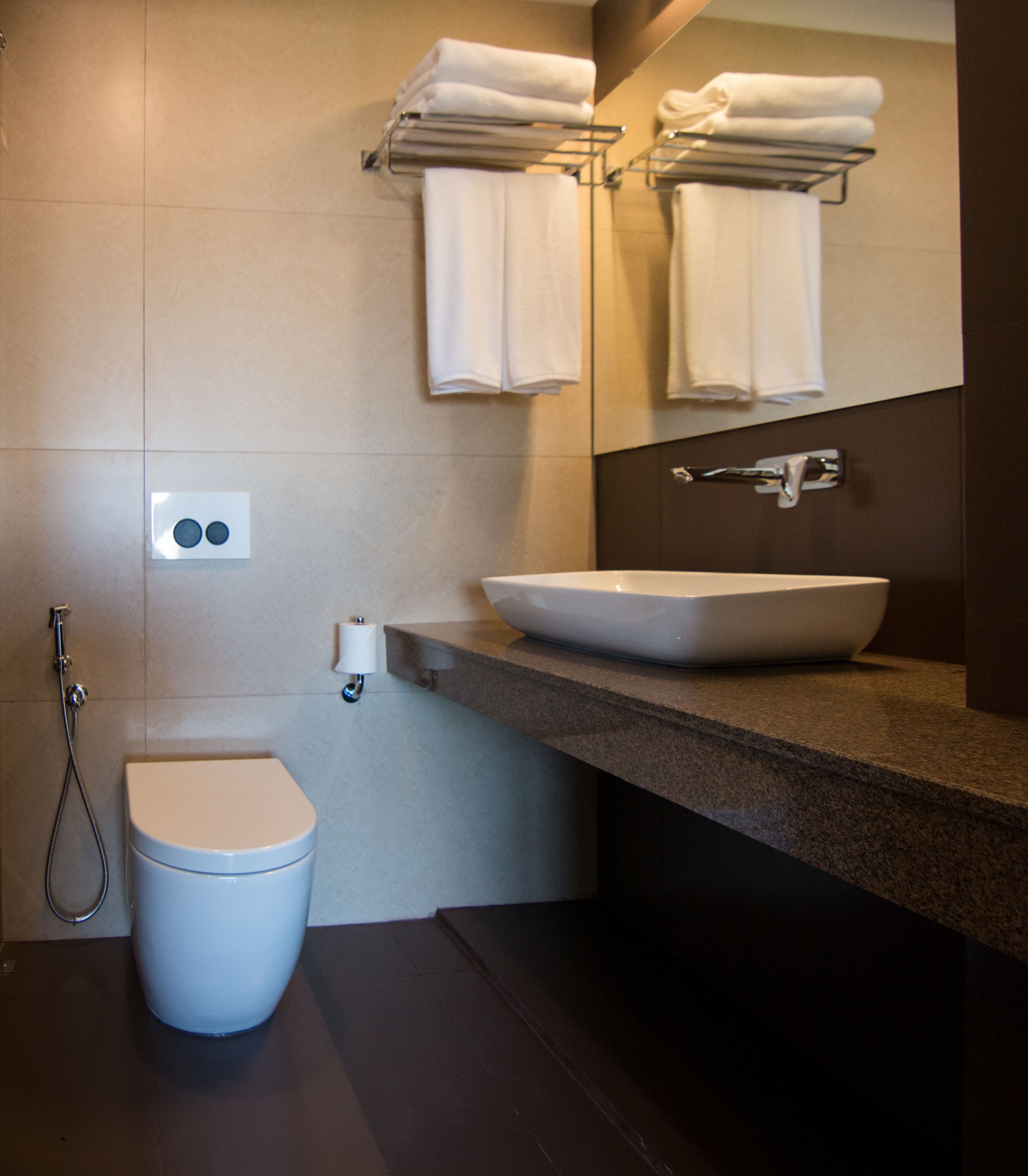 A modern bathroom with a white toilet, a large sink, and a towel rack with folded towels.