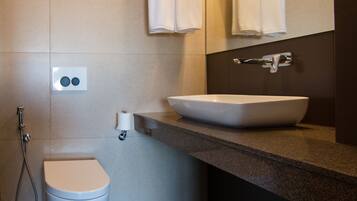 A modern bathroom with a white toilet, a large sink, and a towel rack with folded towels.