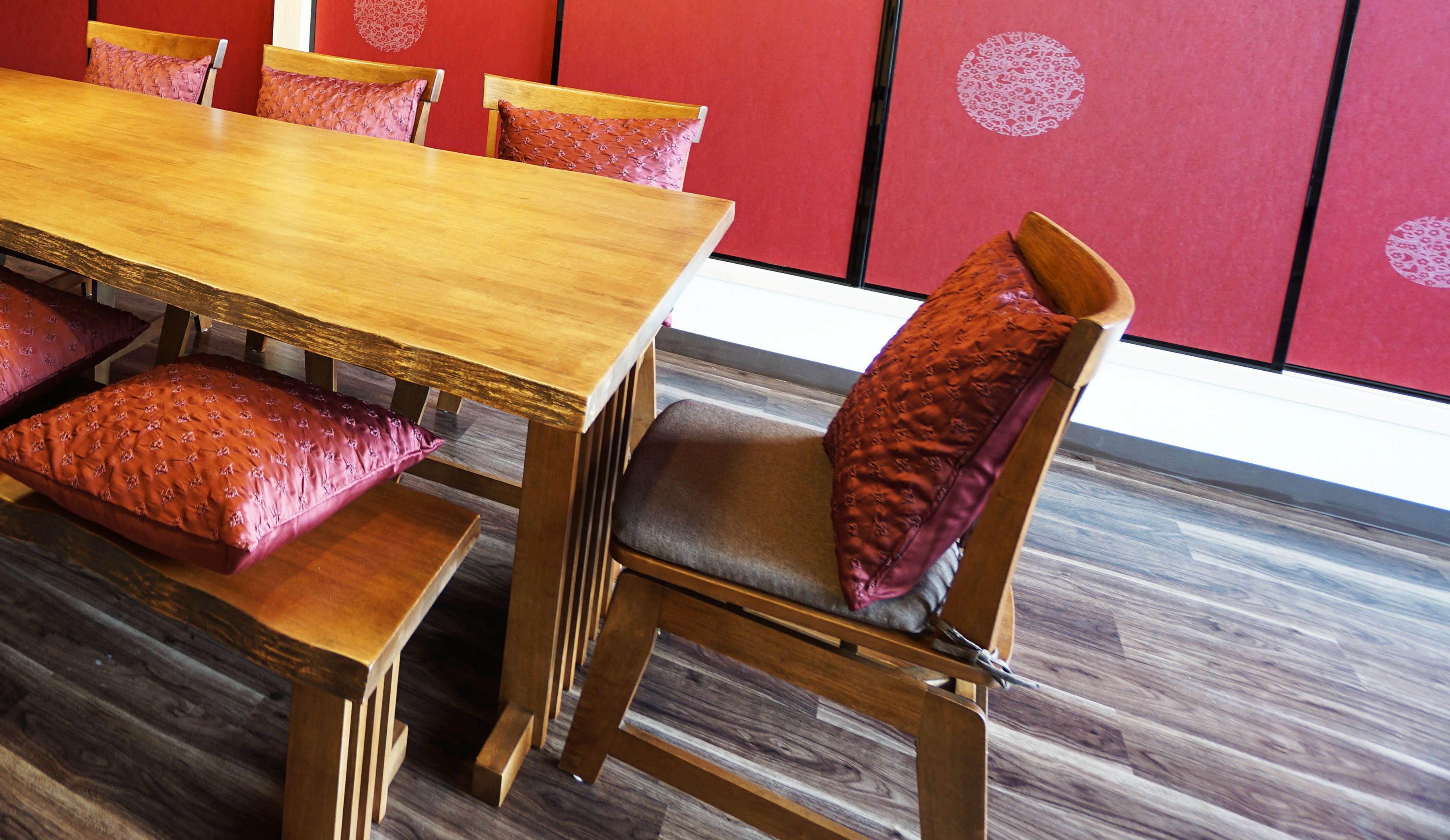 A wooden dining table with matching chairs and red cushions.