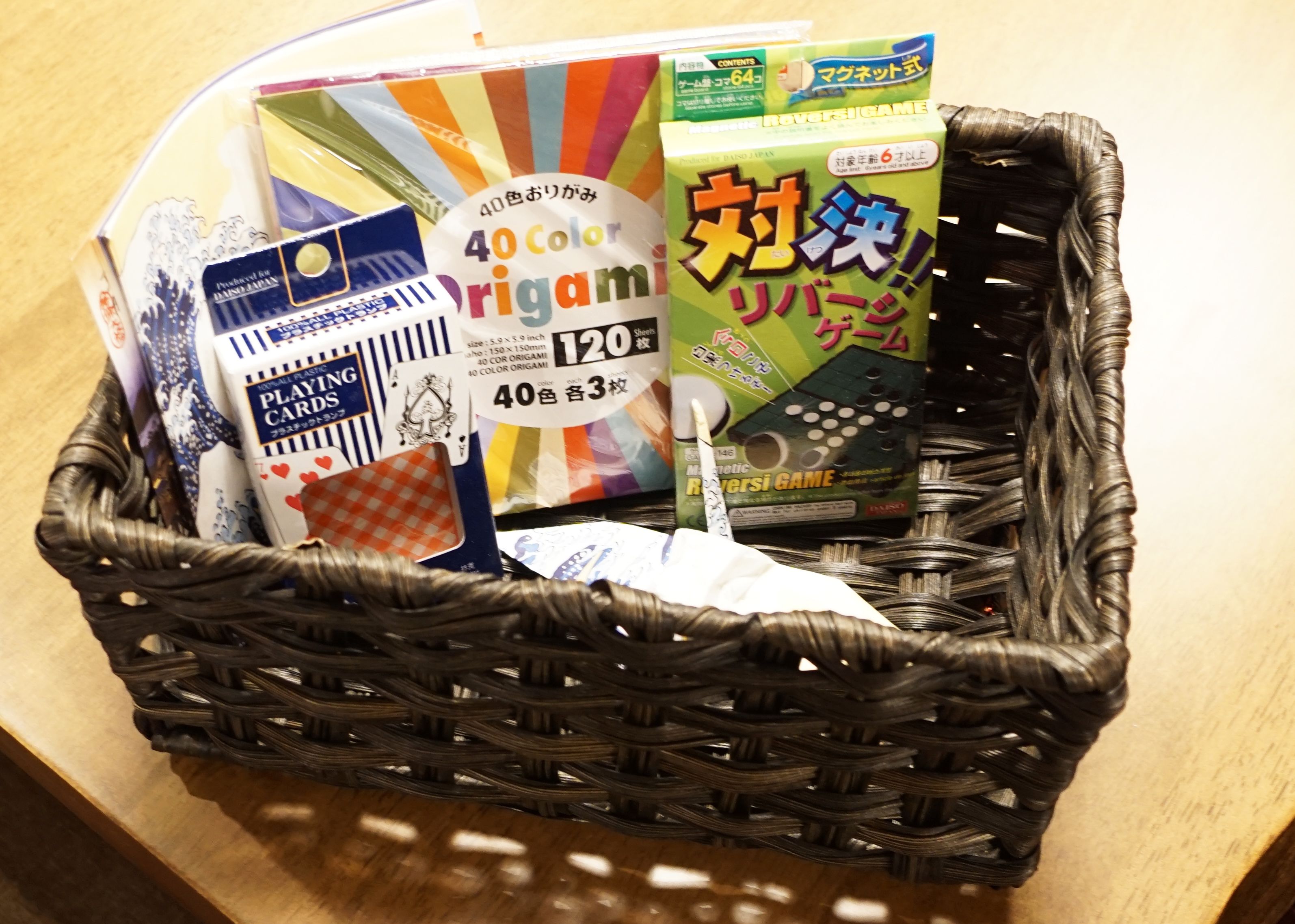 A basket containing origami paper, a deck of cards, and a game box.