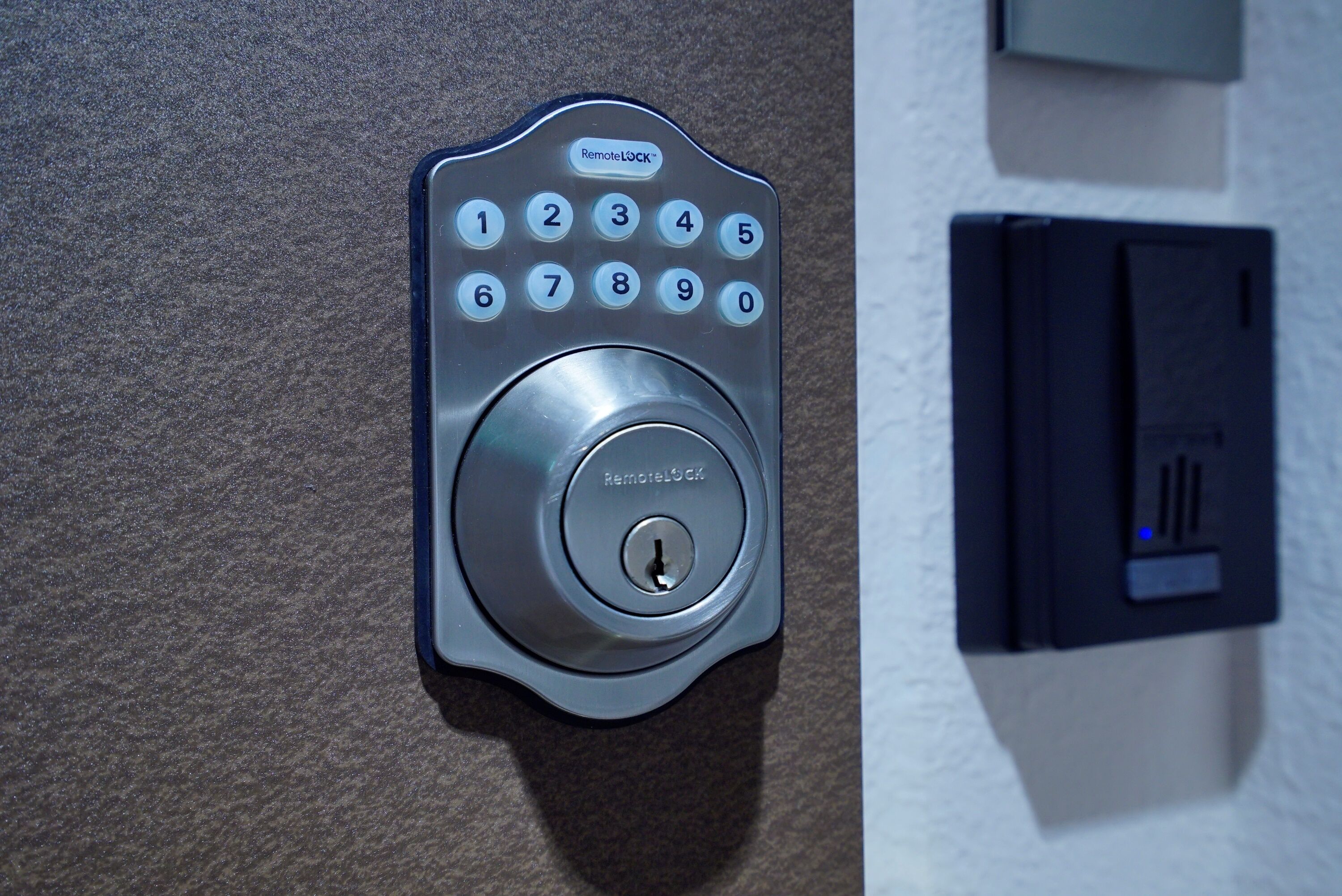 A wall-mounted electronic keypad with a numeric keypad and a central lock button, likely for a door or gate.