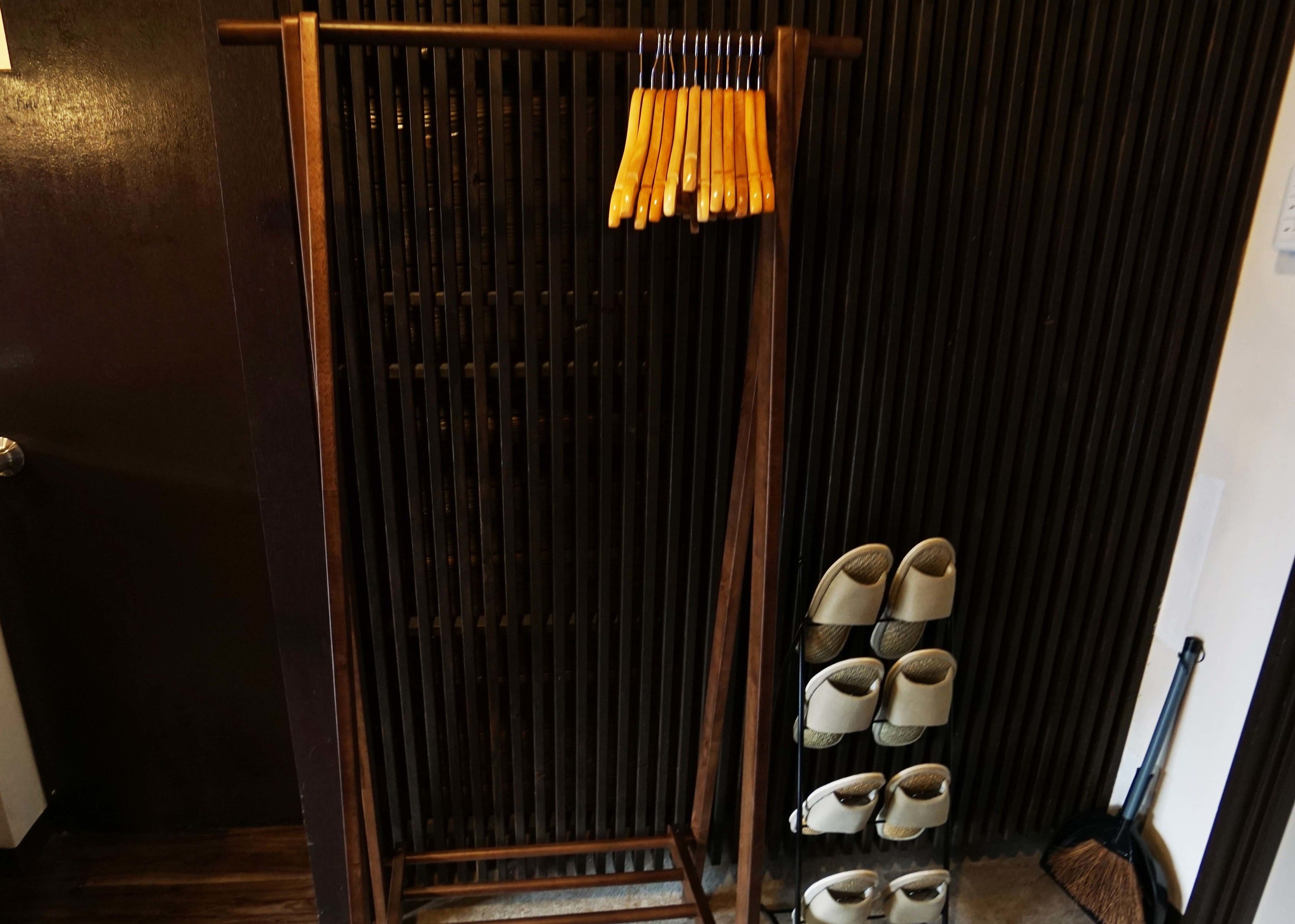 A wooden shoe rack with multiple pairs of shoes and a wooden door with a dark interior.