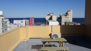 Eine Dachterrasse mit Meerblick, ausgestattet mit einem Tisch und einer Bank, umgeben von Gebäuden.