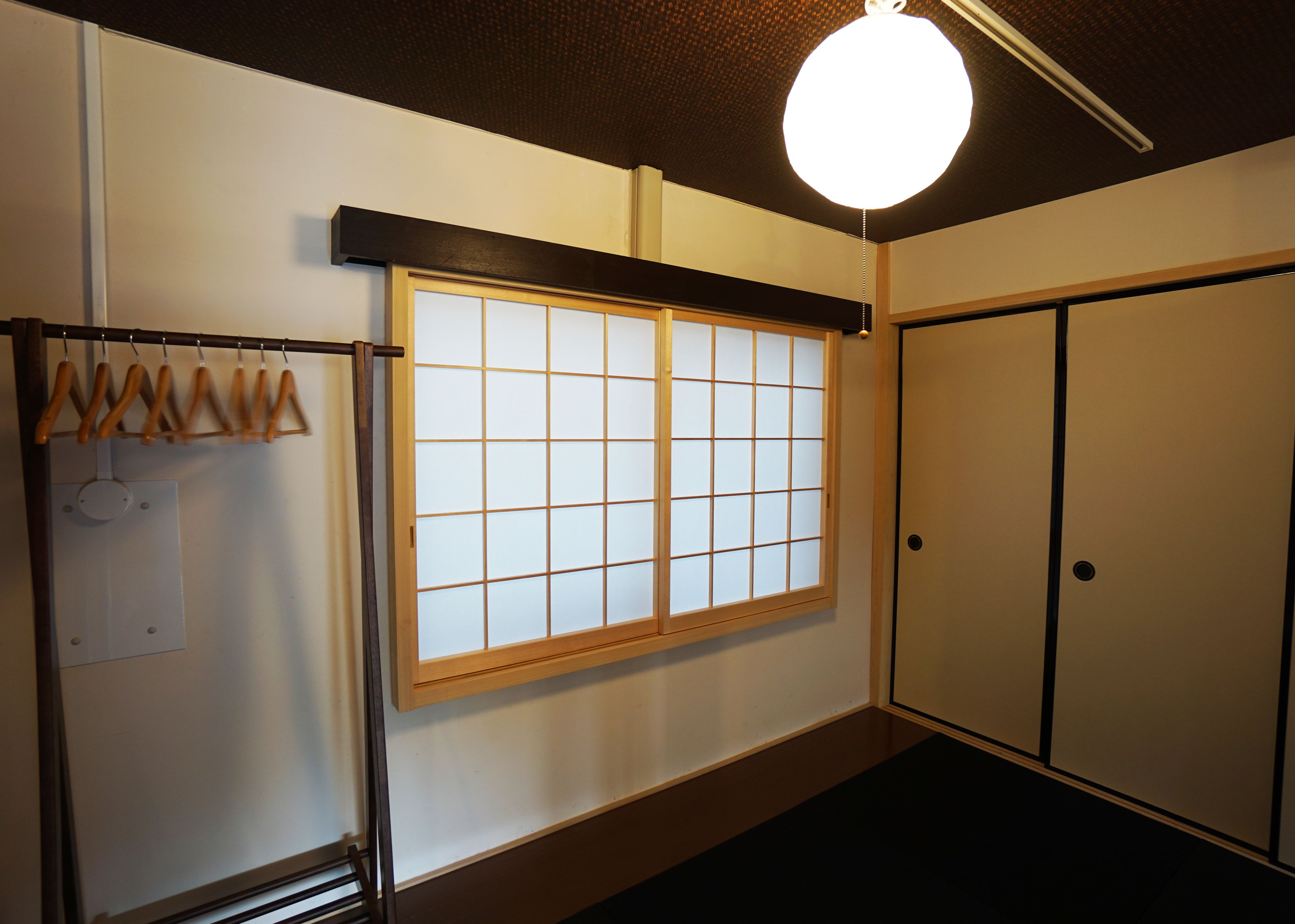 A traditional Japanese room with sliding doors, a shoji screen window, and a hanging wooden rack.