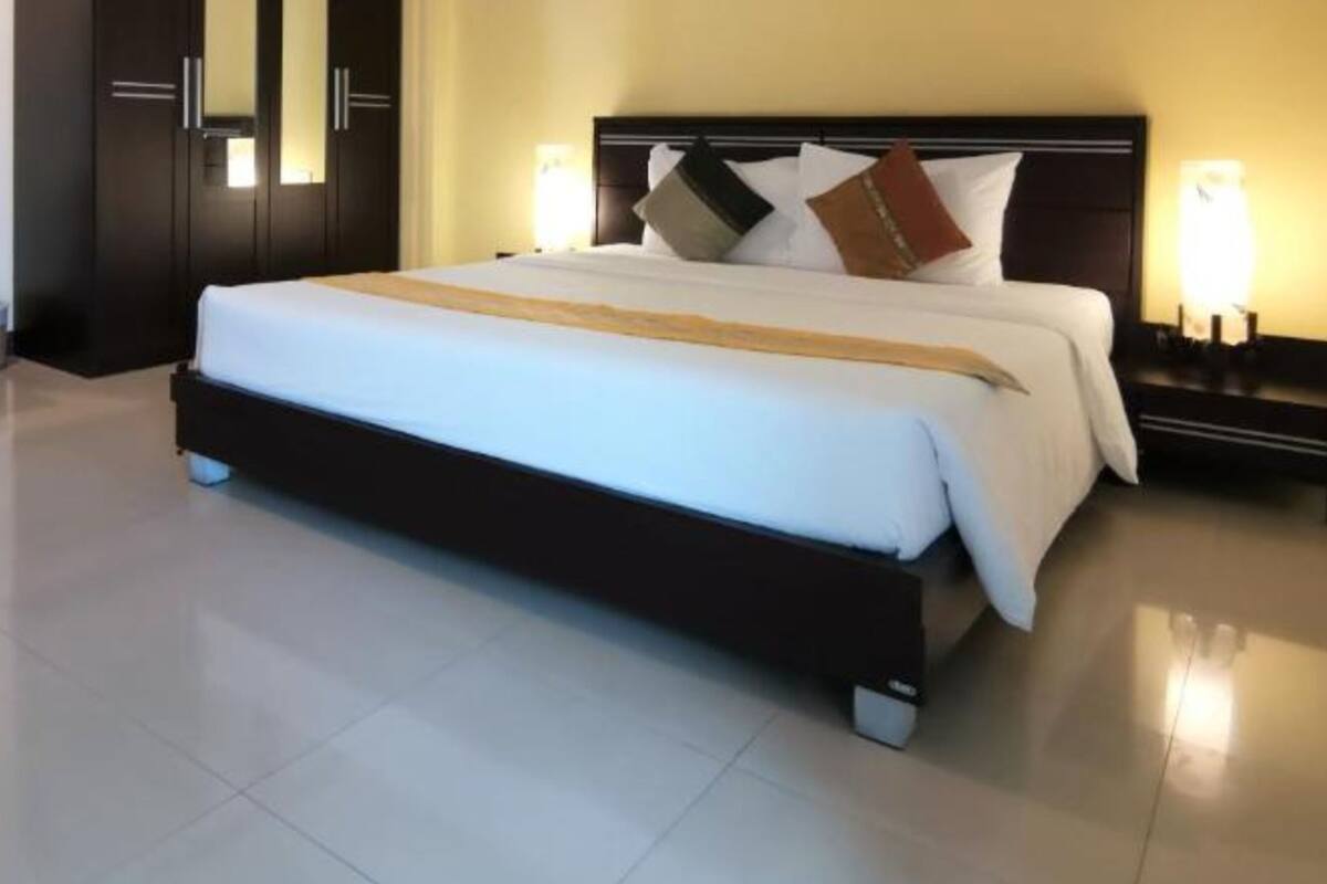 A hotel room with a large bed, a nightstand with a lamp, and a wardrobe.